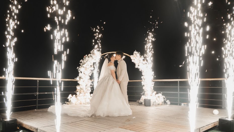 A couple kissing beneath sparklers on a waterfront deck