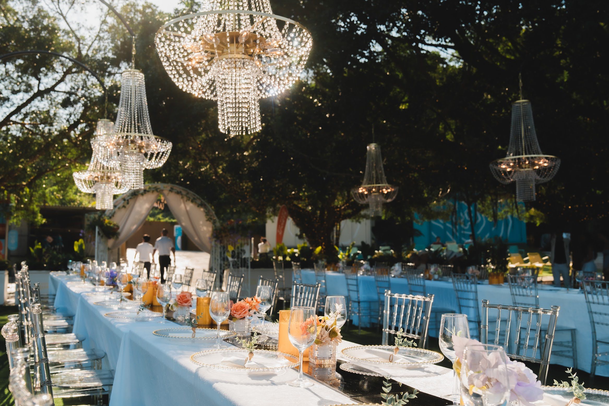 Long dining tables set with flowers under hanging crystal chandeliers